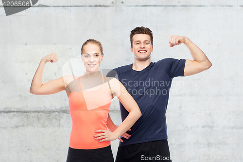 Image of happy sportive man and woman showing biceps power