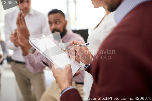 Image of business team and man writing to notepad at office