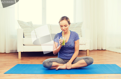 Image of happy woman with smoothie sitting on mat at home