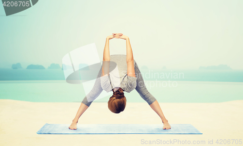 Image of woman making yoga wide-legged forward bend on mat