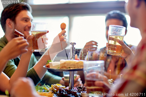 Image of happy friends eating and drinking at bar or pub