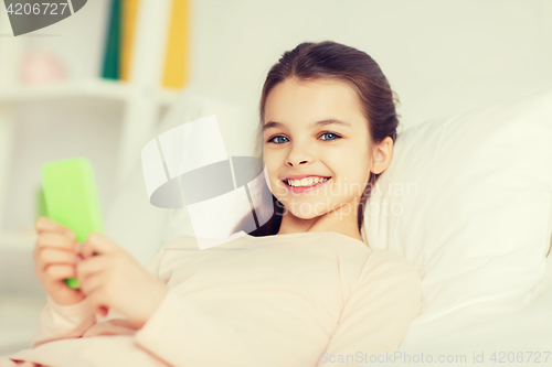 Image of happy girl lying in bed with smartphone at home