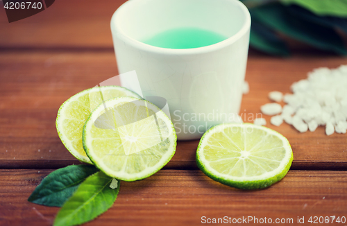 Image of close up of body lotion in cup and limes on wood