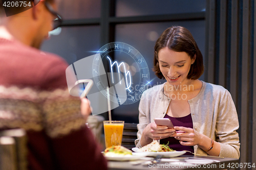 Image of couple with smartphones and zodiac signs at cafe