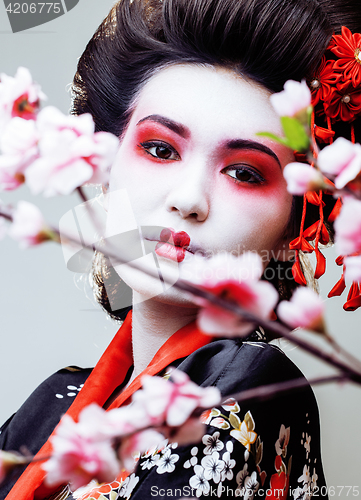 Image of young pretty geisha in black kimono among sakura, asian ethno close up