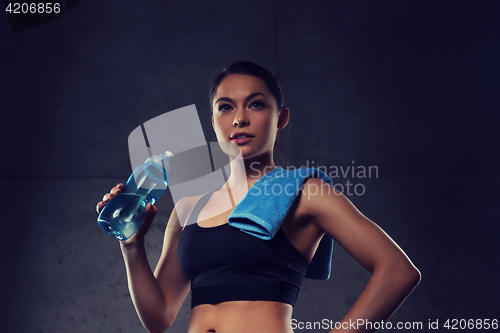 Image of woman with towel drinking water from bottle in gym