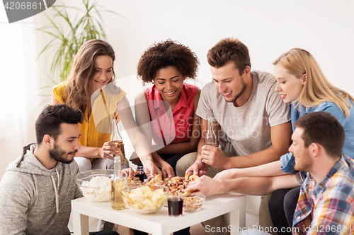 Image of happy friends with drinks eating pizza at home