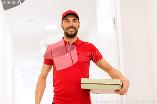 Image of happy delivery man with pizza boxes in corridor