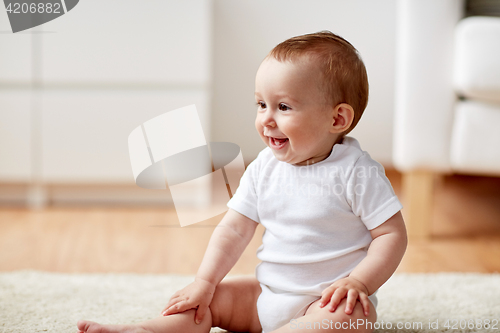 Image of happy baby boy or girl sitting on floor at home