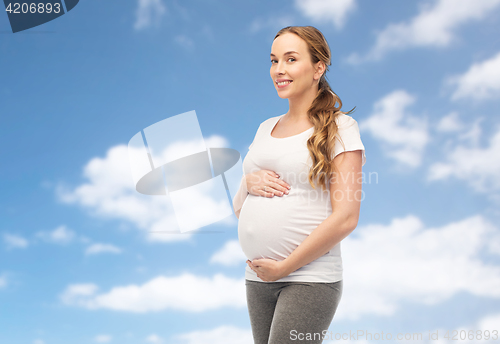 Image of happy pregnant woman touching her belly over sky