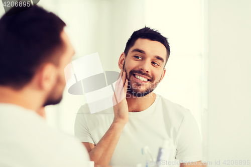 Image of happy young man looking to mirror at home bathroom