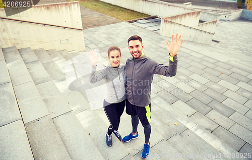Image of happy couple waving hands outdoors on city street