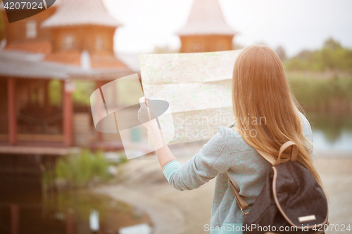 Image of Back side of traveler girl searching right direction on map, orange sunset light, traveling along Europe