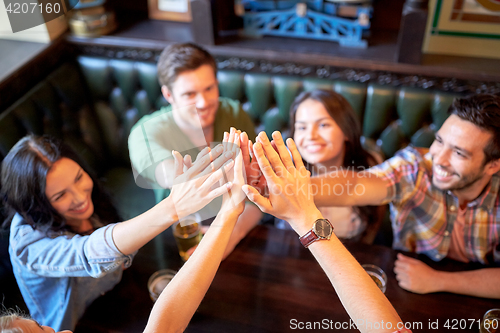 Image of friends drinking beer and making high five at bar
