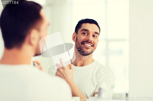 Image of man with perfume looking to mirror at bathroom