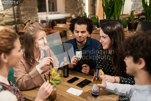 Image of friends with drinks, money and bill at bar