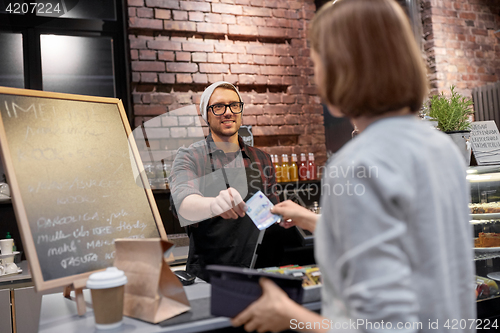 Image of happy barman and woman paying money at cafe