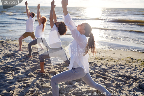 Image of group of people making yoga exercises on beach