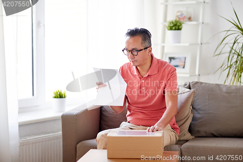 Image of man with parcel box reading invoice at home