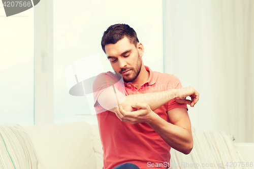 Image of unhappy man suffering from pain in hand at home