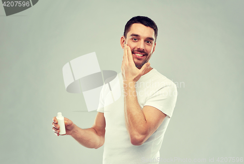 Image of happy young man applying cream or lotion to face