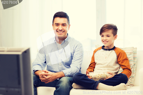 Image of smiling father and son watching tv at home