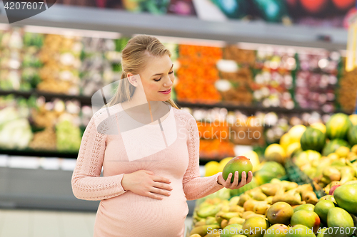 Image of happy pregnant woman with mango at grocery store