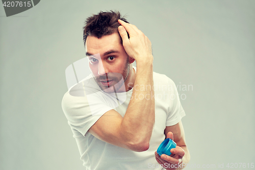 Image of happy young man styling his hair with wax or gel