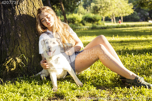 Image of young attractive blond woman playing with her dog in green park at summer, lifestyle people concept