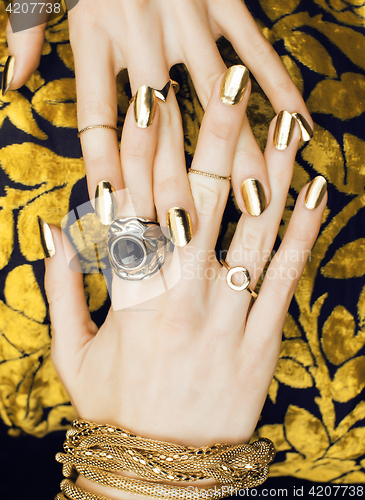 Image of woman hands with golden manicure lot of jewelry on fancy dress close up