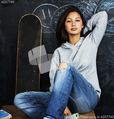 Image of young cute teenage girl in classroom at blackboard seating on ta