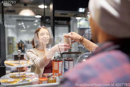 Image of happy woman taking coffee cup from seller at cafe