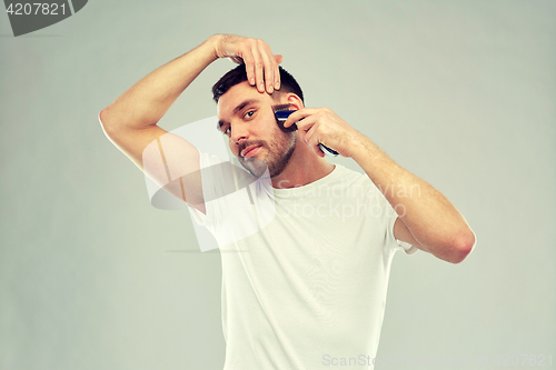 Image of smiling man shaving beard with trimmer over gray