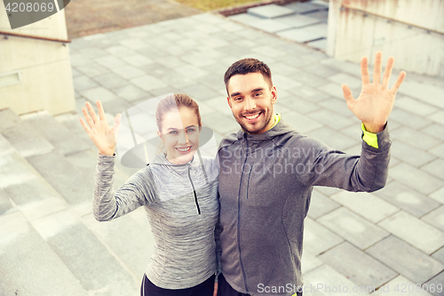 Image of happy couple waving hands outdoors on city street