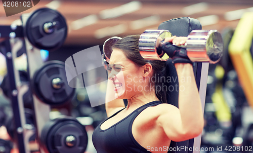 Image of young woman flexing muscles with dumbbell in gym