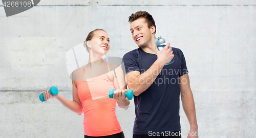 Image of sportive man and woman with dumbbell and water