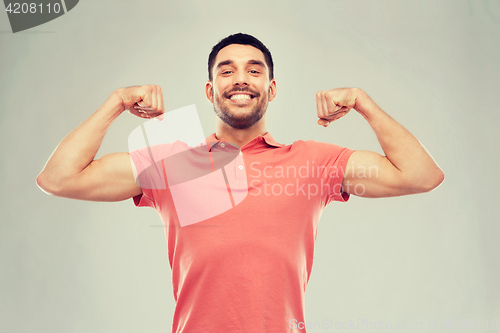 Image of smiling man showing biceps over gray background