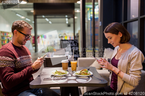 Image of happy couple with smartphones at vegan restaurant