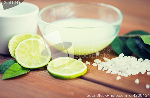 Image of close up of body lotion in bowl and limes on wood