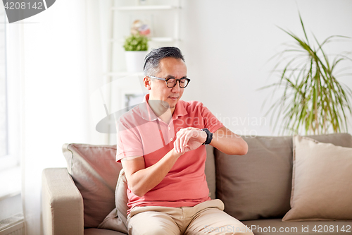 Image of asian man checking time on wristwatch at home