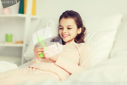 Image of happy girl lying in bed with smartphone at home