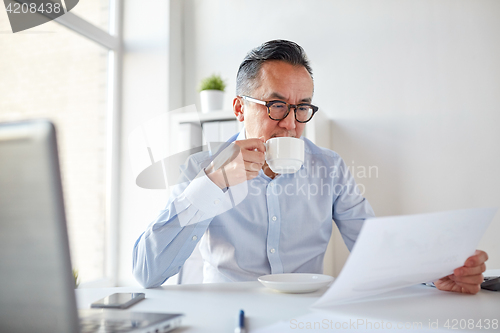 Image of businessman with papers drinking coffee at office