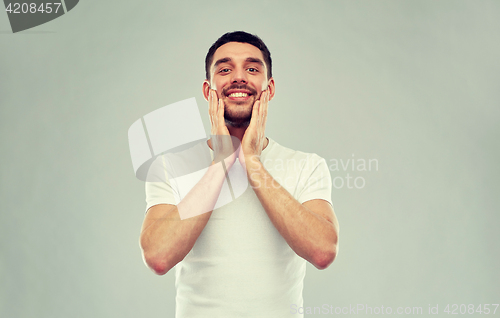 Image of happy young man applying aftershave to face