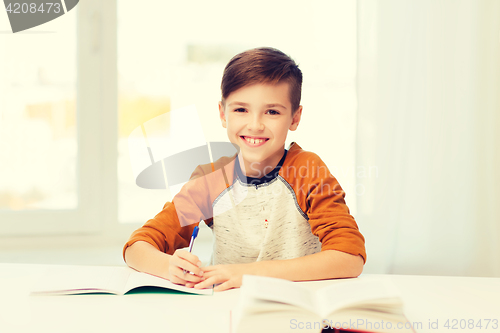 Image of smiling student boy writing to notebook at home