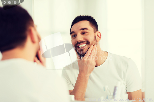 Image of happy young man looking to mirror at home bathroom