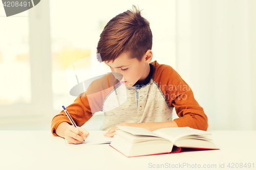 Image of student boy with book writing to notebook at home