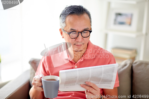 Image of man drinking tea and reading newspaper at home