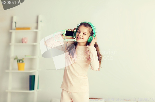 Image of girl jumping on bed with smartphone and headphones