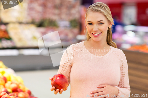 Image of happy pregnant woman with apple at grocery store