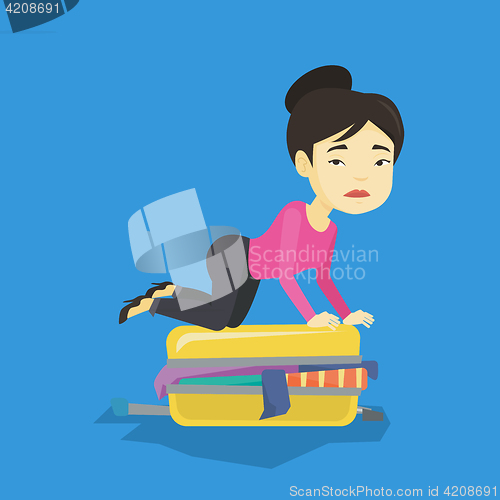 Image of Young woman trying to close suitcase.